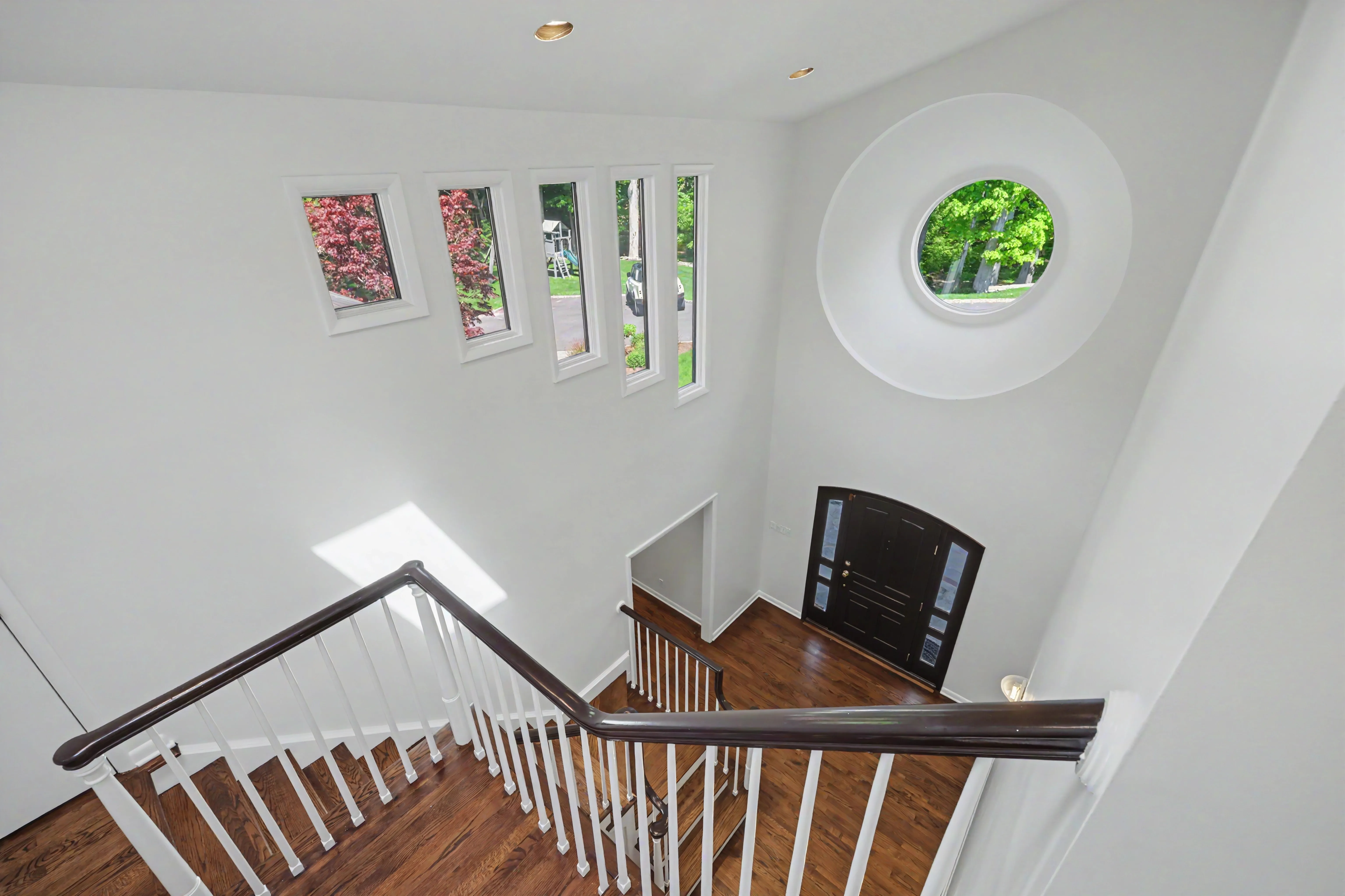 Staircase landing looking down to foyer — circular porthole window, hardwood floors, real estate photography Westchester County NY