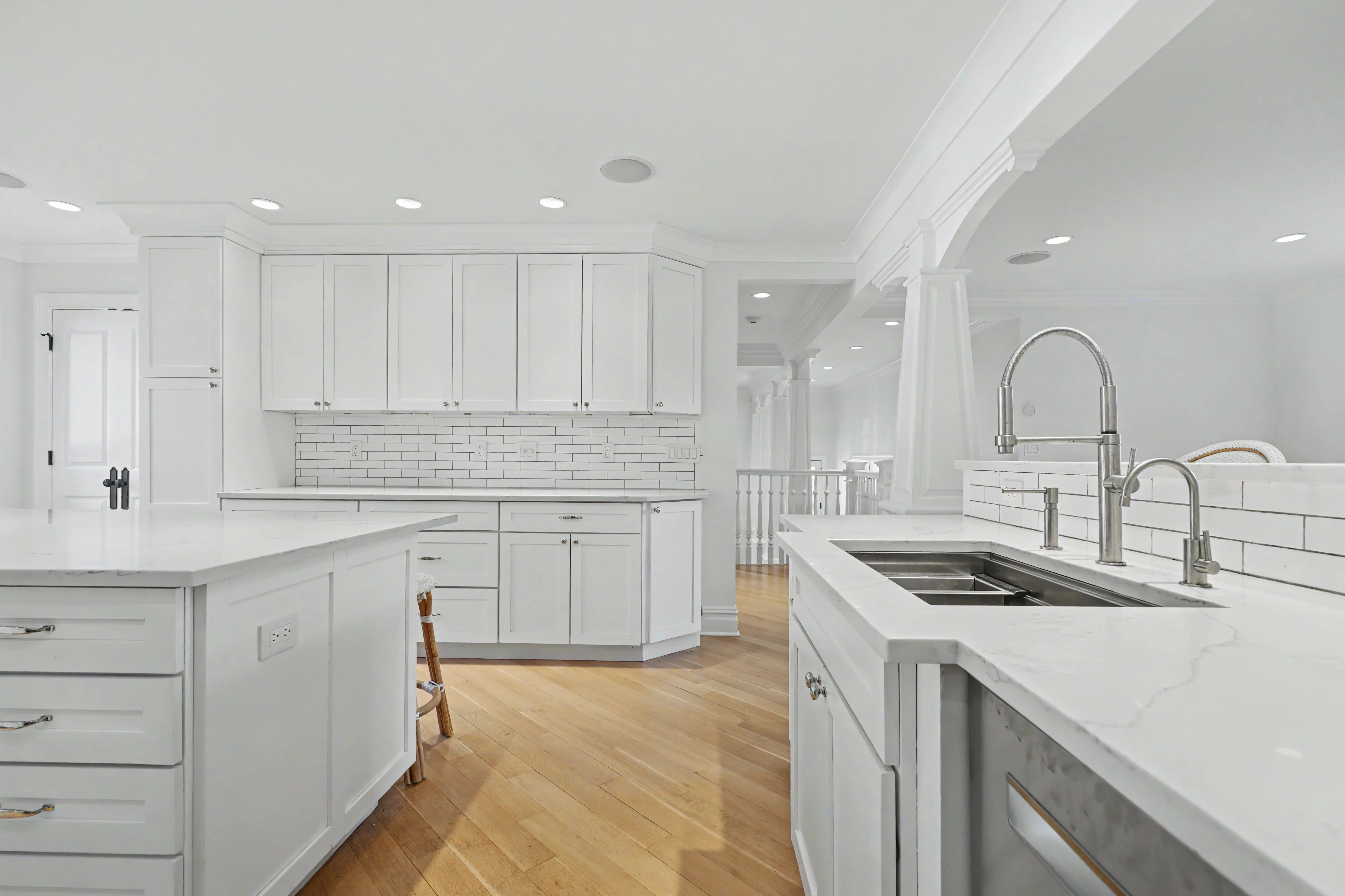 Expansive white kitchen with quartz island and subway tile backsplash, open to great room — real estate listing photography
